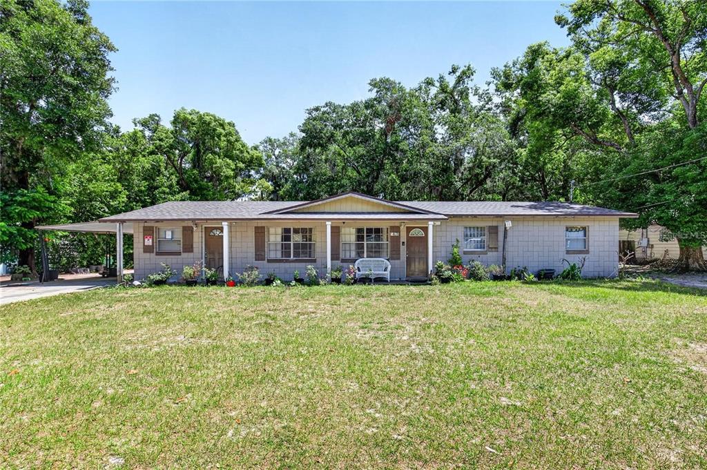 A single-story house with a light-colored block exterior, a covered porch, and mature trees — 1400 N SIMPSON STREET, MOUNT DORA, FL