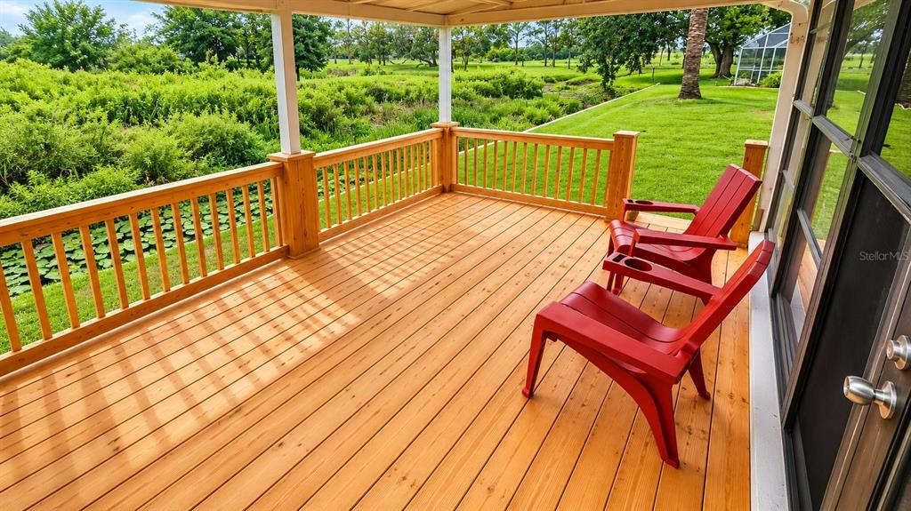 A wooden deck features two red chairs and a railing overlooking a grassy yard — 13036 TOPFLITE COURT, HUDSON, FL