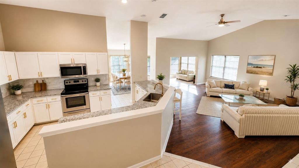 An open-concept living area features a kitchen with white cabinets, a breakfast bar, and hardwood floors — 13036 TOPFLITE COURT, HUDSON, FL