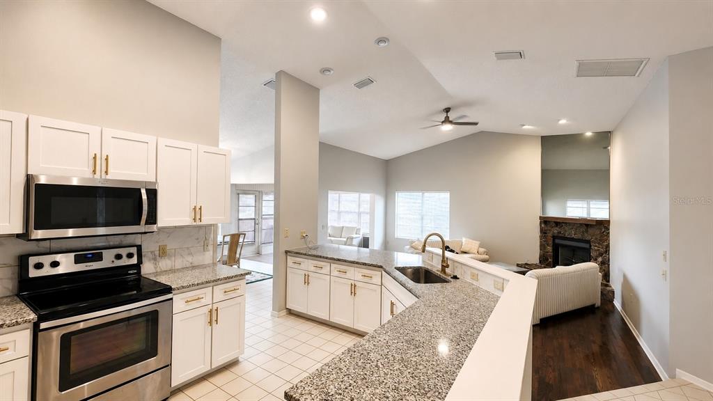 An open-concept kitchen with white cabinets and granite countertops overlooks a living room area — 13036 TOPFLITE COURT, HUDSON, FL