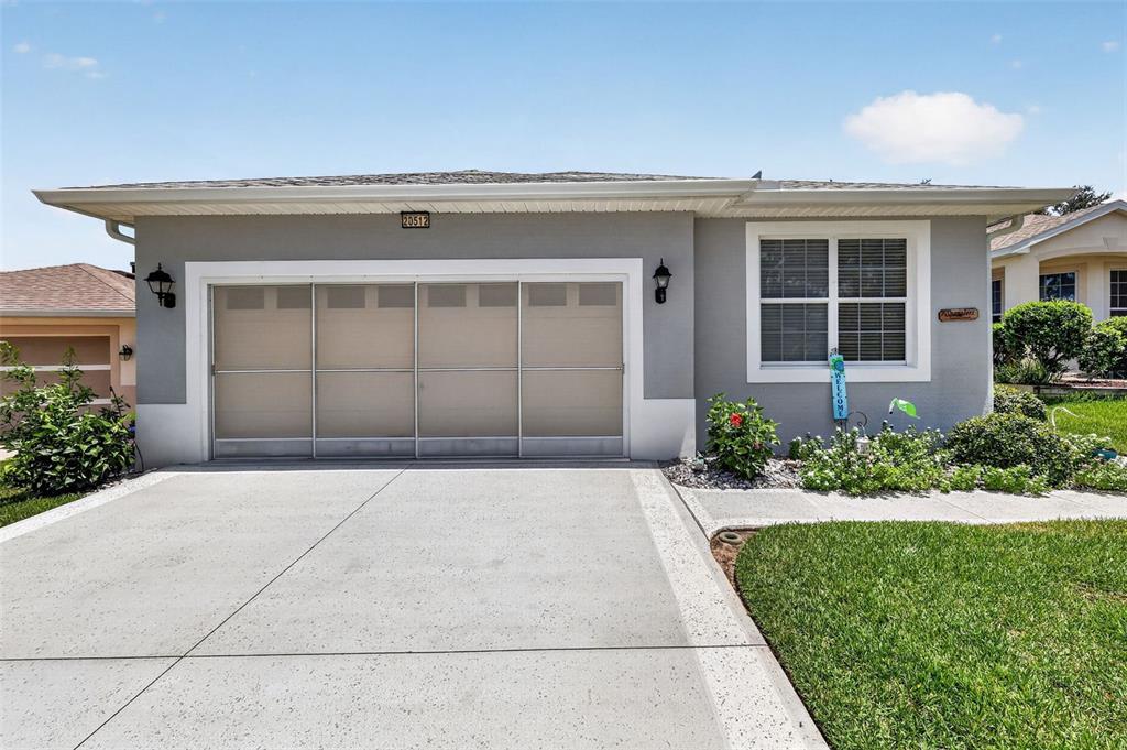 A single-story house exterior features a gray stucco facade, a two-car garage, and a window — 20512 QUEEN ALEXANDRA DRIVE, LEESBURG, FL