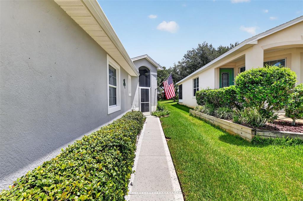 A concrete walkway leads between two houses with green landscaping and an American flag — 20512 QUEEN ALEXANDRA DRIVE, LEESBURG, FL