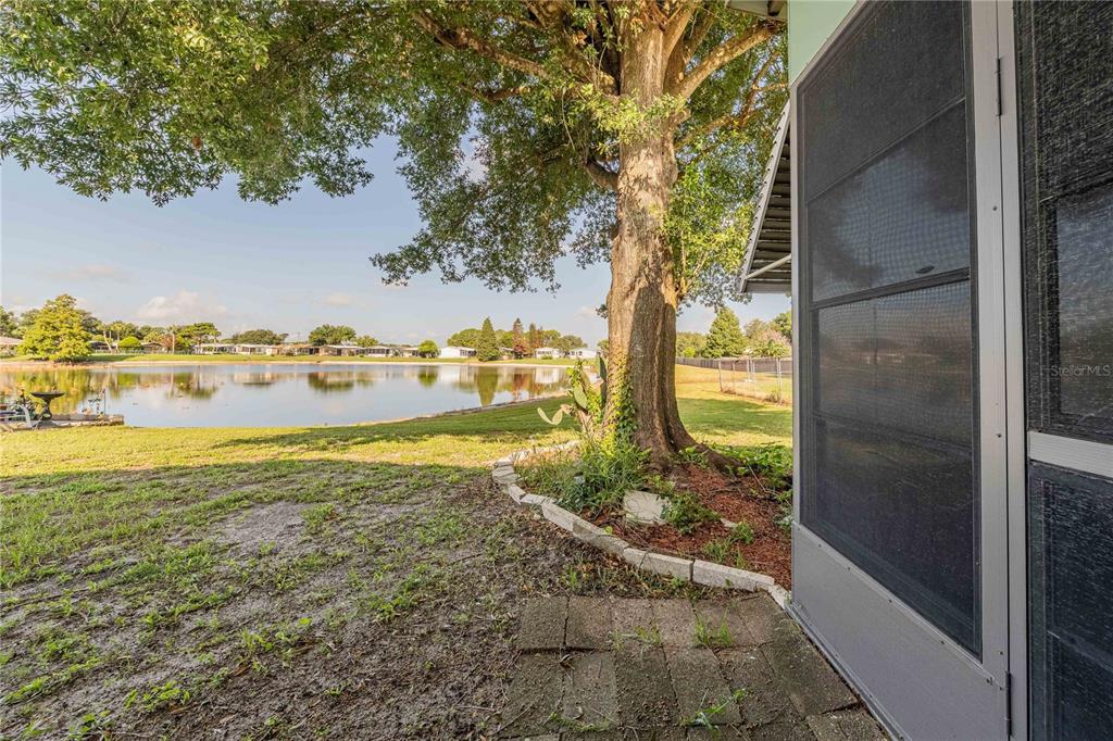 A view of a grassy yard and a pond from a screened-in patio area — 489 VILLAGE CIRCLE SW, WINTER HAVEN, FL
