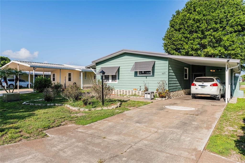 A green single-story house with a carport and a white car parked in the driveway — 489 VILLAGE CIRCLE SW, WINTER HAVEN, FL