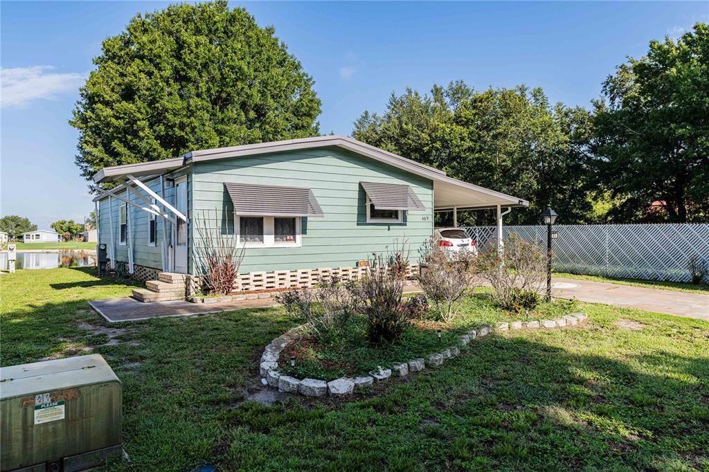 A light green single-story house with a carport and a stone-bordered garden bed — 489 VILLAGE CIRCLE SW, WINTER HAVEN, FL
