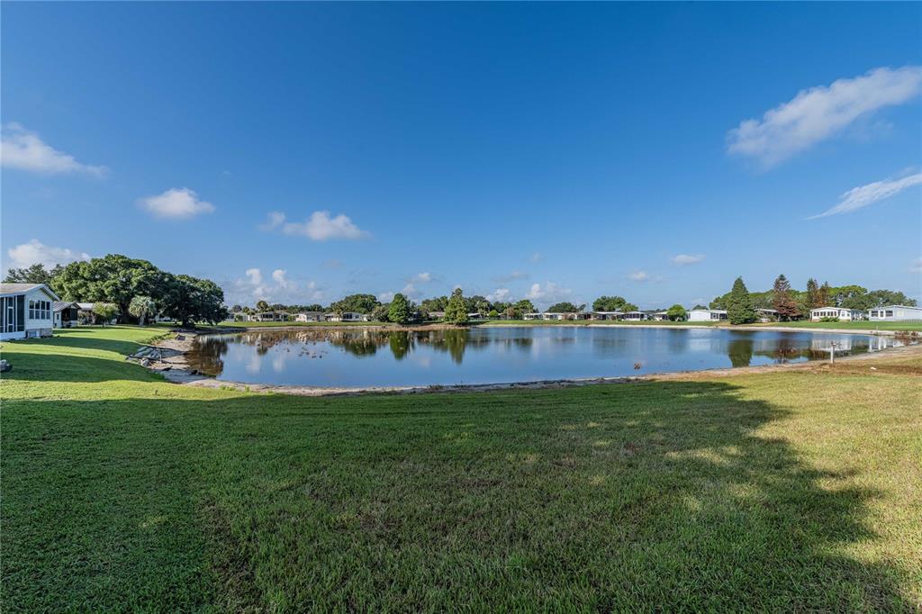 A grassy lawn slopes down toward a pond surrounded by trees and residential homes — 489 VILLAGE CIRCLE SW, WINTER HAVEN, FL