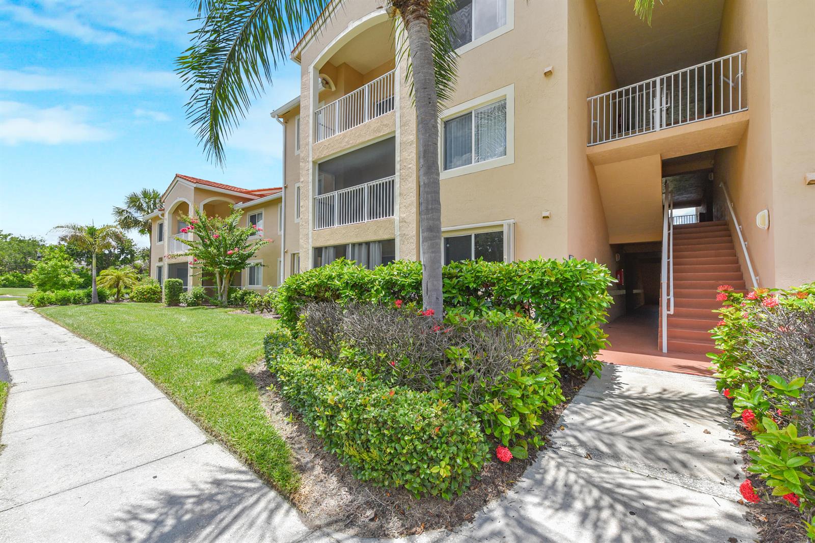 A multi-story apartment building with tan stucco walls, screened balconies, and a concrete staircase — 1590 S 42nd Circle # 106, Vero Beach FL 32967, VERO BEACH, FL