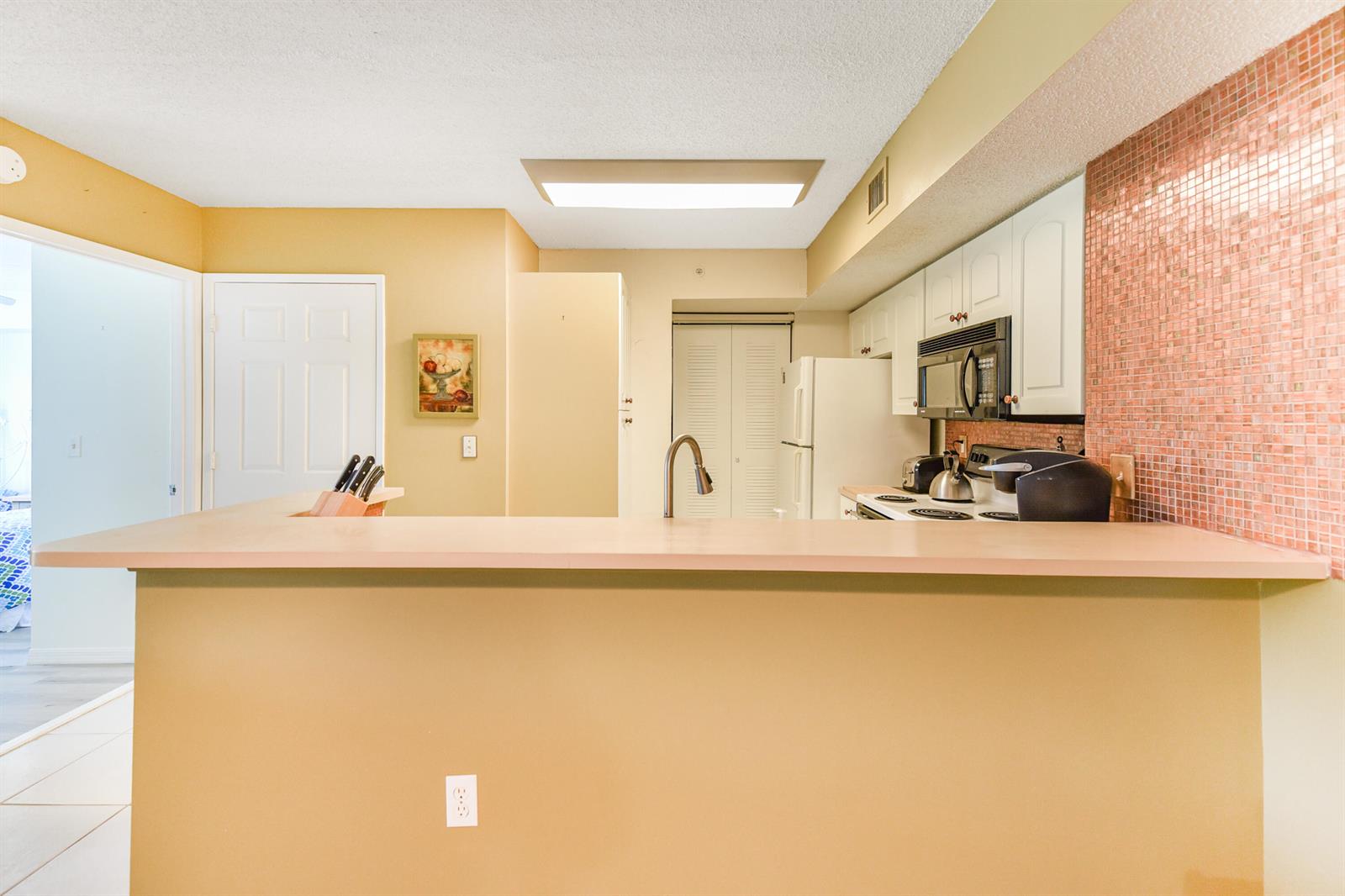 A kitchen features a breakfast bar, white cabinets, a pink tiled backsplash, and beige walls — 1590 S 42nd Circle # 106, Vero Beach FL 32967, VERO BEACH, FL
