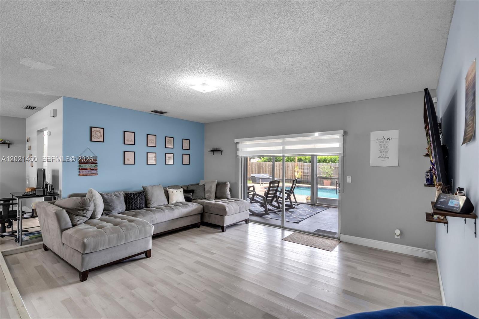 A living room features a grey sectional sofa, light wood floors, and sliding doors to a pool — 850 NW 79th Ave, Margate FL 33063, MARGATE, FL