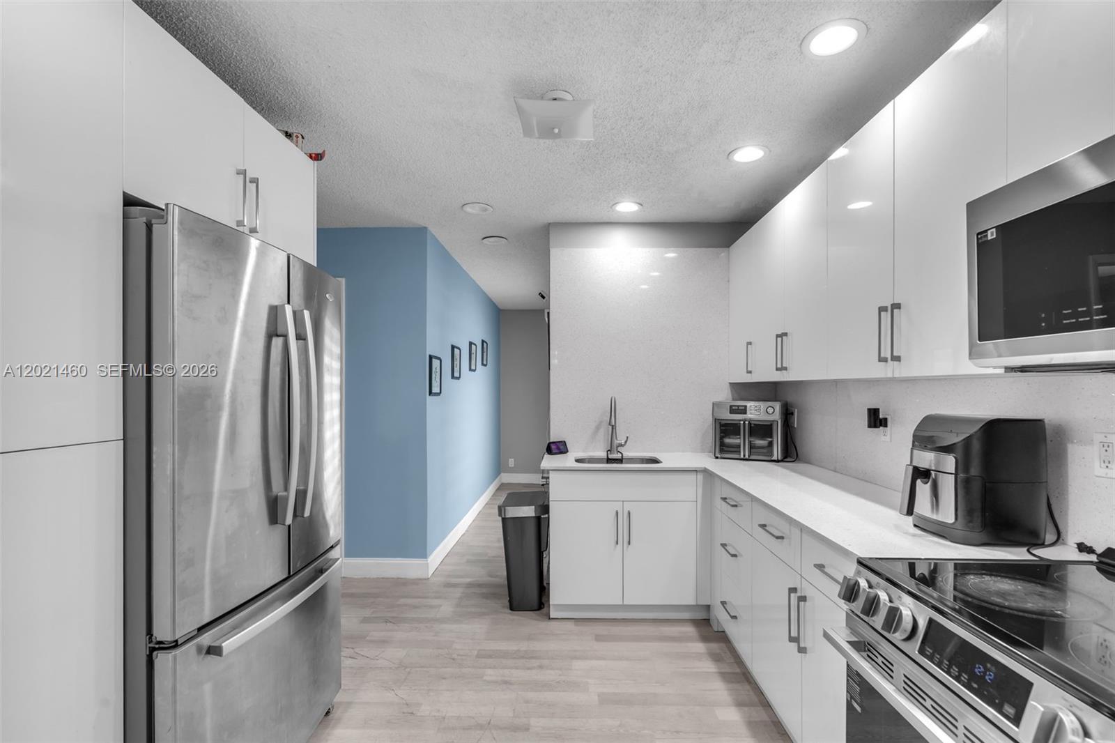 A modern kitchen features white cabinetry, stainless steel appliances, and a blue accent wall — 850 NW 79th Ave, Margate FL 33063, MARGATE, FL