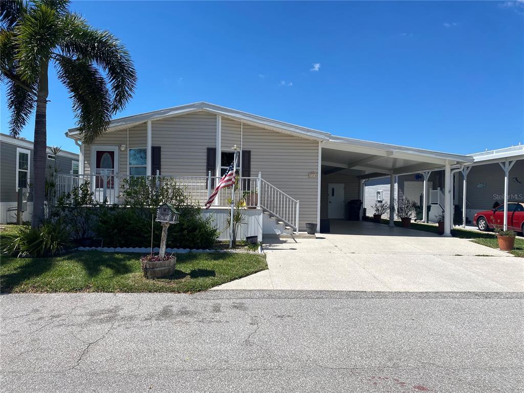 A single-story manufactured home with light siding, a front porch, and an attached carport — 724 BLACKBURN BOULEVARD, NORTH PORT, FL