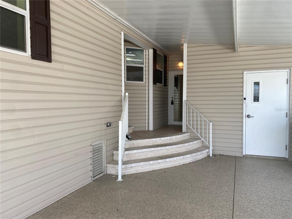 A covered concrete patio features curved brick steps leading to a white entry door — 724 BLACKBURN BOULEVARD, NORTH PORT, FL