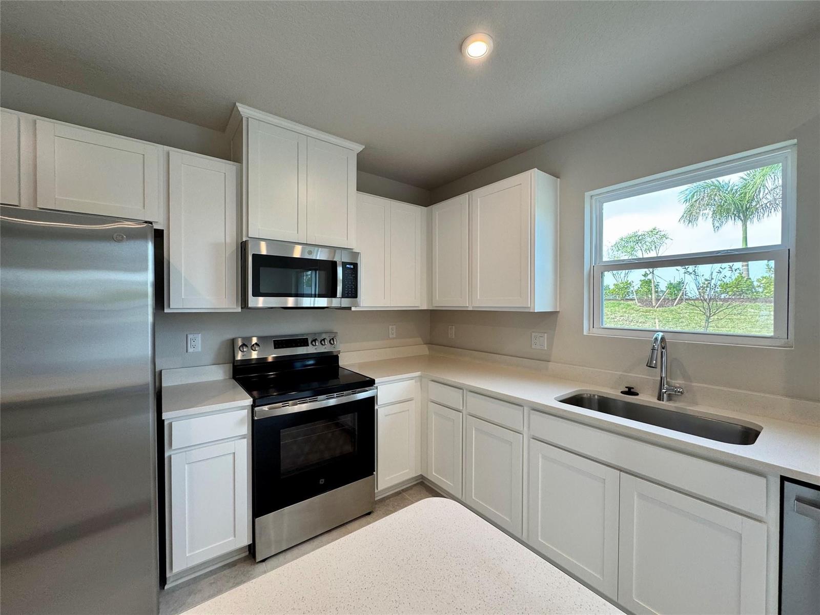 A kitchen features white cabinets, stainless steel appliances, quartz countertops, and a window over the sink — PORT ST. LUCIE, FL