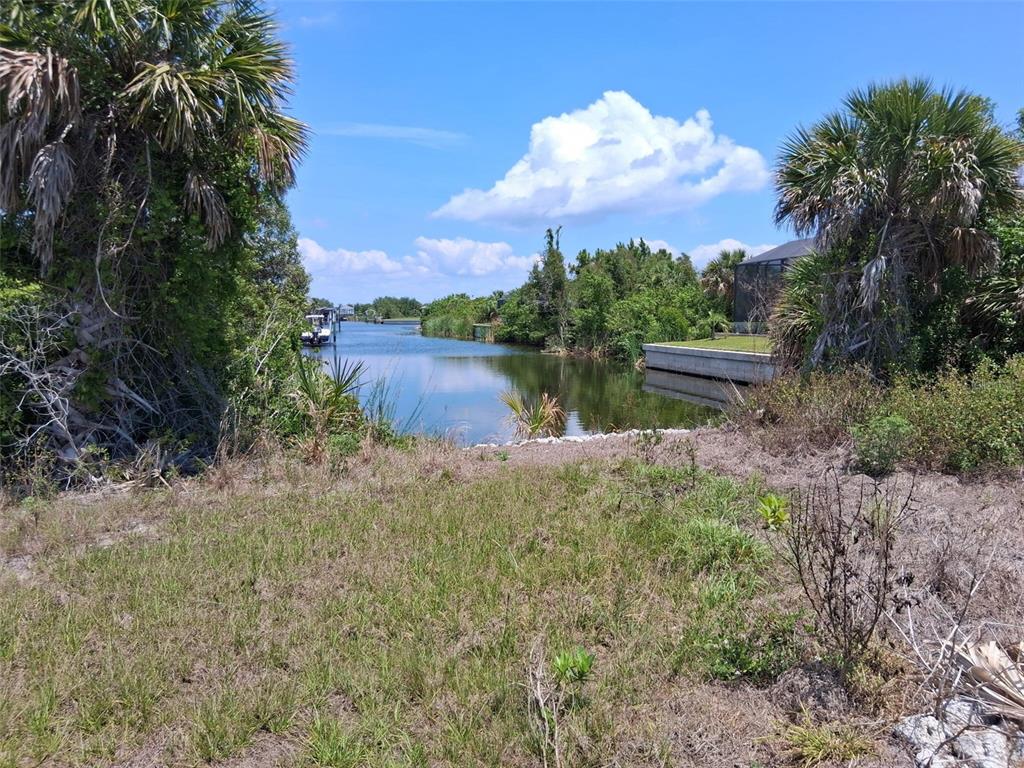 A grassy lot overlooks a narrow canal lined with palm trees and a residential property — 10166 KINGSVILLE DRIVE, PORT CHARLOTTE, FL