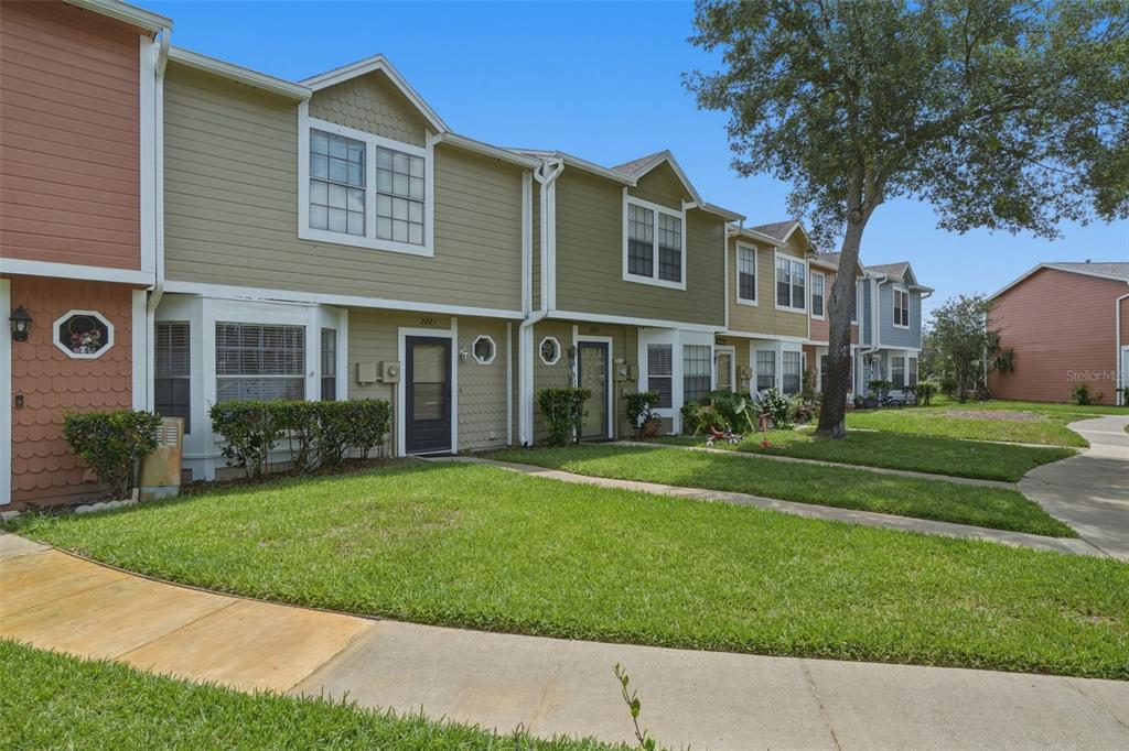 A row of two-story townhomes with green siding and front lawns under a blue sky — 2025 WATERLEAF STREET, ORLANDO, FL