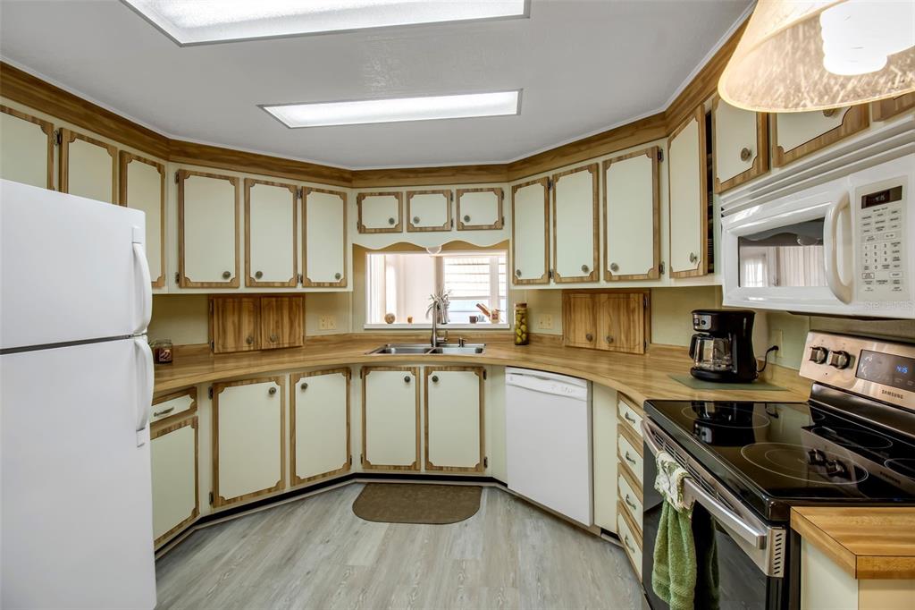 A kitchen features light-colored cabinets with wood trim, laminate countertops, and white appliances — 5619 BAYSHORE ROAD UNIT 160, PALMETTO, FL
