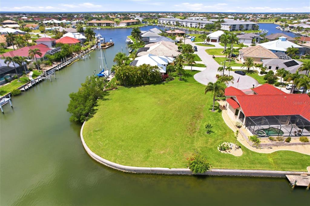 An aerial view shows a vacant waterfront lot next to a house with a pool — 1501 ORIOLE COURT, PUNTA GORDA, FL