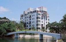 A white multi-story apartment building stands behind a curved pedestrian bridge over a canal — 2421 Lake Pancoast Dr # 3B, Miami Beach FL 33140, MIAMI BEACH, FL