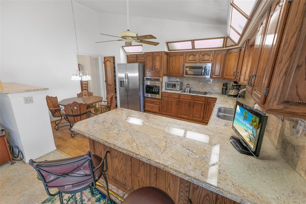A kitchen features wood cabinets, granite countertops, stainless steel appliances, and an adjacent dining area — 4801 S PENINSULA DRIVE, PONCE INLET, FL