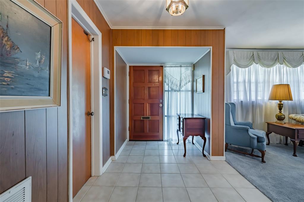 An entryway with wood-paneled walls, tile flooring, and a wooden front door leads to a living area — 5004 S HESPERIDES STREET, TAMPA, FL