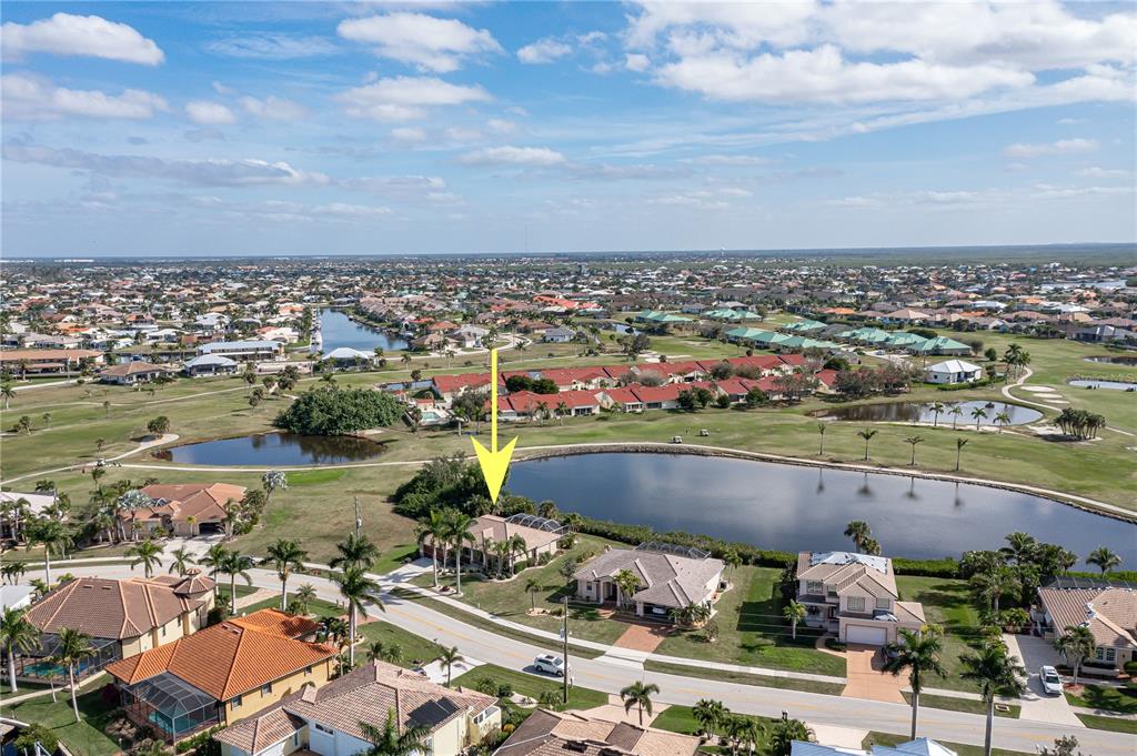 An aerial view shows a residential house with a pool cage beside a pond — 4077 LA COSTA ISLAND COURT, PUNTA GORDA, FL