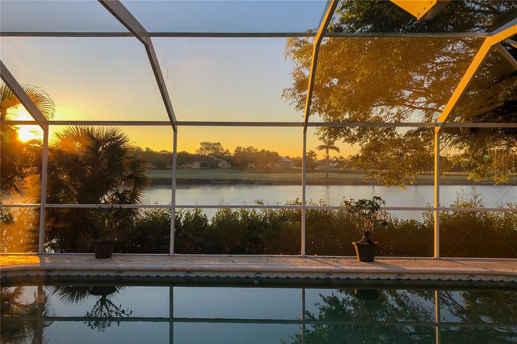A swimming pool view from a screened-in lanai overlooks a lake at sunset — 4077 LA COSTA ISLAND COURT, PUNTA GORDA, FL