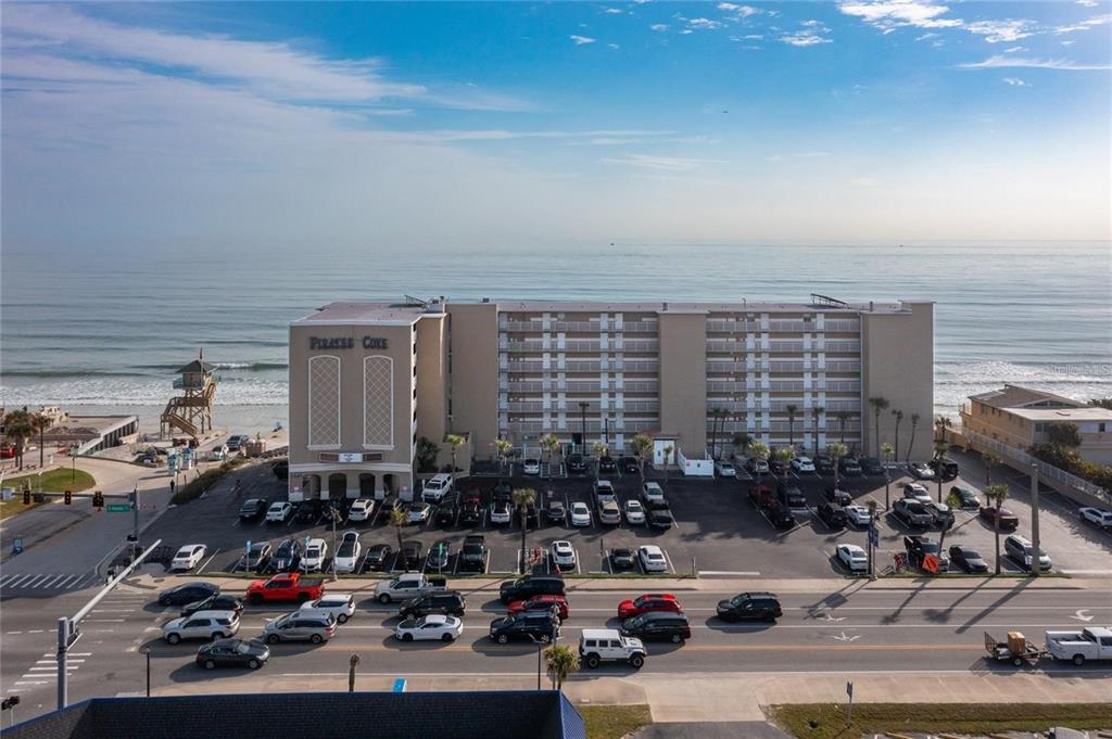 An aerial view shows the exterior of the Pirates Cove beachfront condominium complex and parking lot — 3501 S ATLANTIC AVENUE UNIT 5200, DAYTONA BEACH, FL