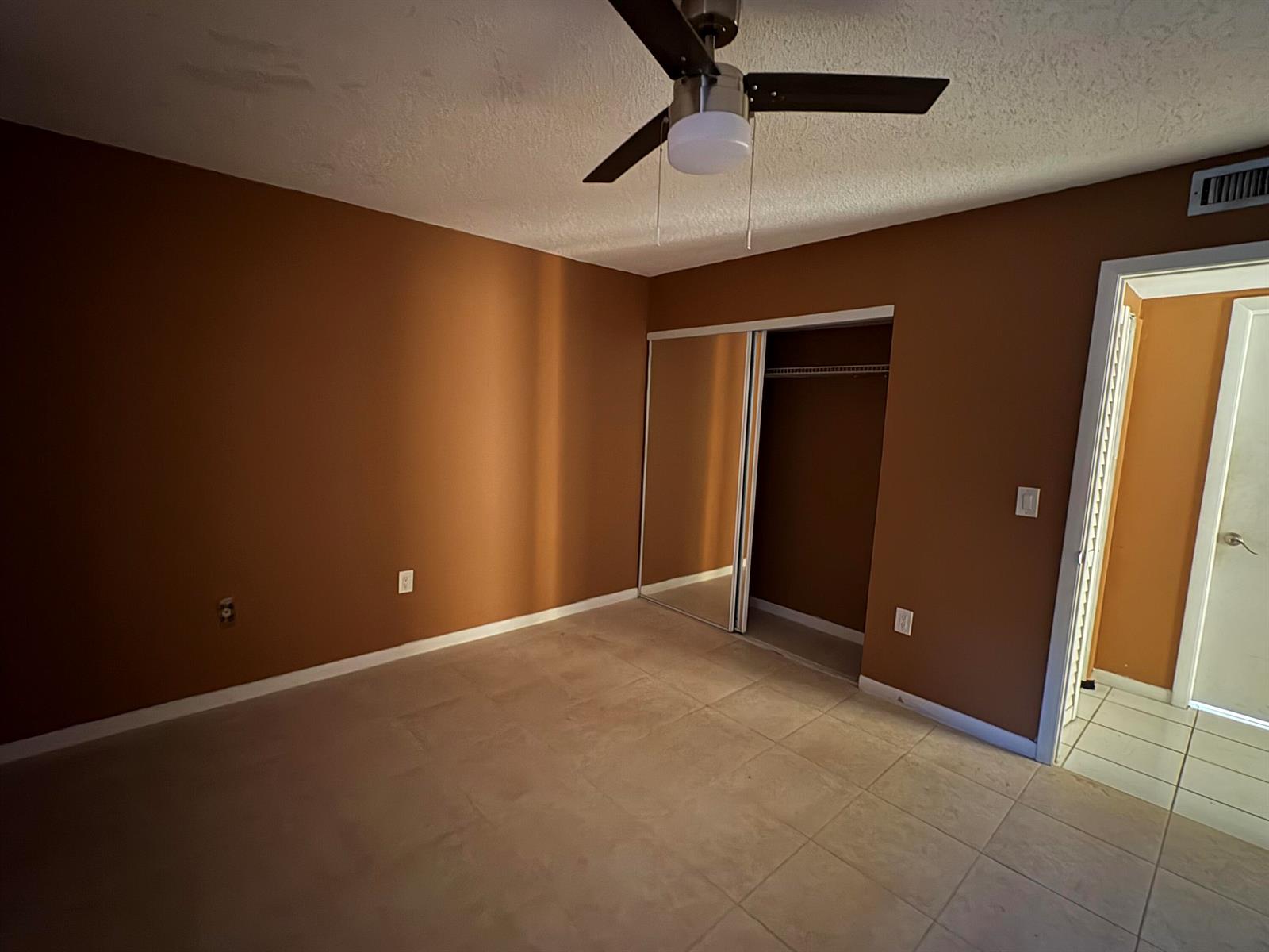 An empty bedroom features brown walls, tile flooring, a ceiling fan, and a mirrored closet — 650 SW 2nd Avenue # 2460, Boca Raton FL 33432, BOCA RATON, FL