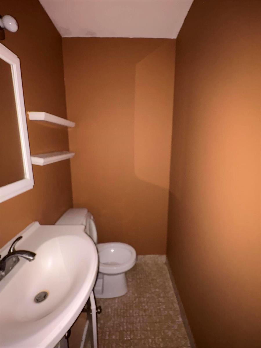 A small bathroom features brown walls, a white pedestal sink, a toilet, and wall shelving — 650 SW 2nd Avenue # 2460, Boca Raton FL 33432, BOCA RATON, FL