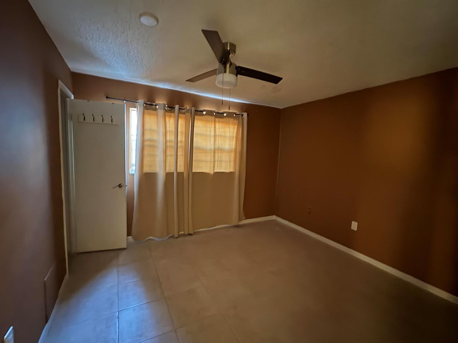 An empty bedroom features brown walls, tiled flooring, a ceiling fan, and beige curtains — 650 SW 2nd Avenue # 2460, Boca Raton FL 33432, BOCA RATON, FL