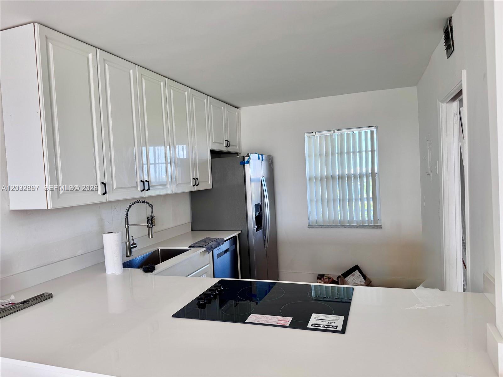 A kitchen features white cabinets, a stainless steel refrigerator, and a black glass cooktop — 575 Oaks Ln # 1008, Pompano Beach FL 33069, POMPANO BEACH, FL