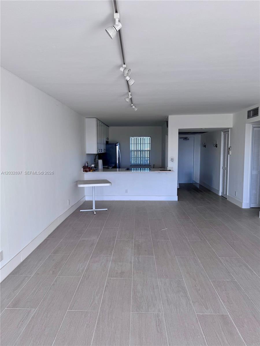 An open-concept living area features light-colored tile flooring, a track lighting system, and a kitchen — 575 Oaks Ln # 1008, Pompano Beach FL 33069, POMPANO BEACH, FL