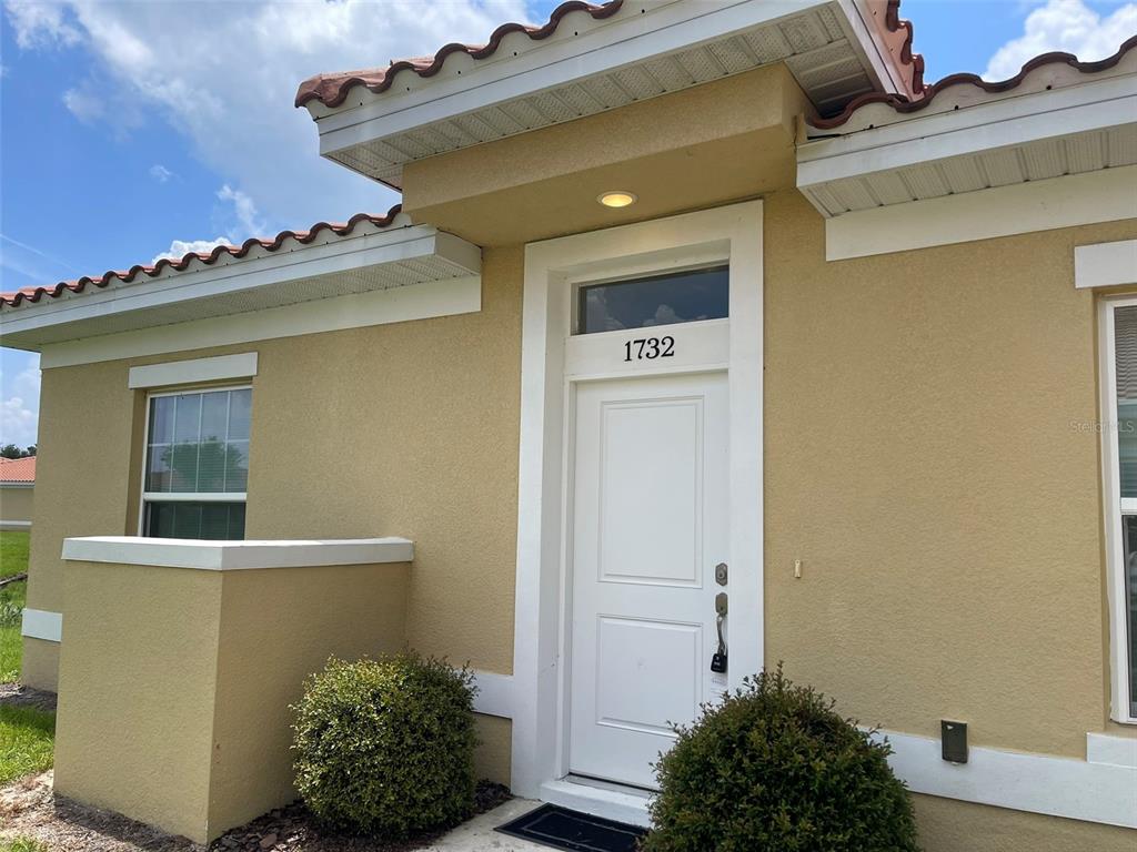 The exterior of a tan stucco house features a white front door and red roof tiles — 1732 PACIFIC ROAD, POINCIANA, FL