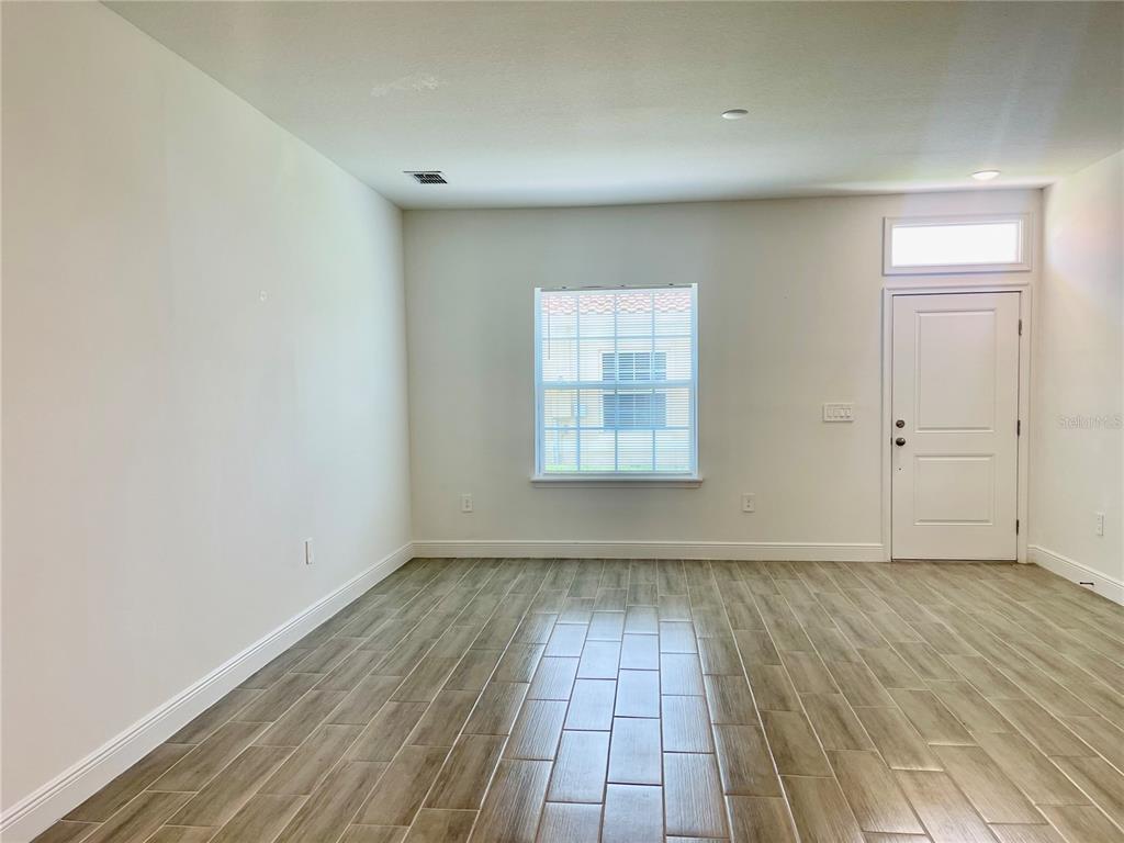 An empty room features light-colored walls, wood-look tile flooring, a single window, and a door — 1732 PACIFIC ROAD, POINCIANA, FL