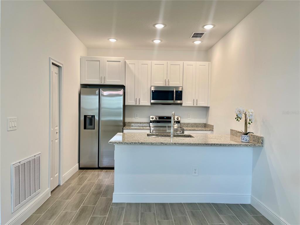 A kitchen features white cabinets, stainless steel appliances, granite countertops, and light wood-look tile flooring — 1732 PACIFIC ROAD, POINCIANA, FL