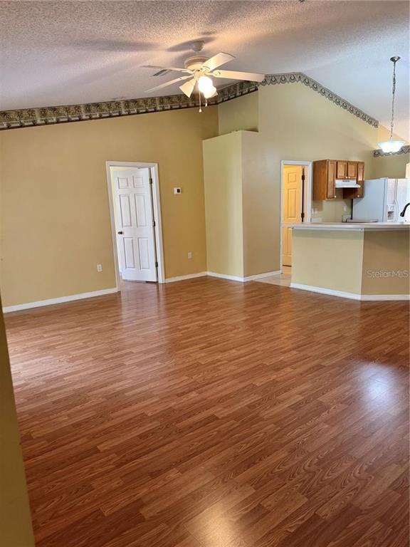 A living room with wood-look flooring, vaulted ceilings, a ceiling fan, and an adjacent kitchen — 15 PRATTWOOD LANE, PALM COAST, FL