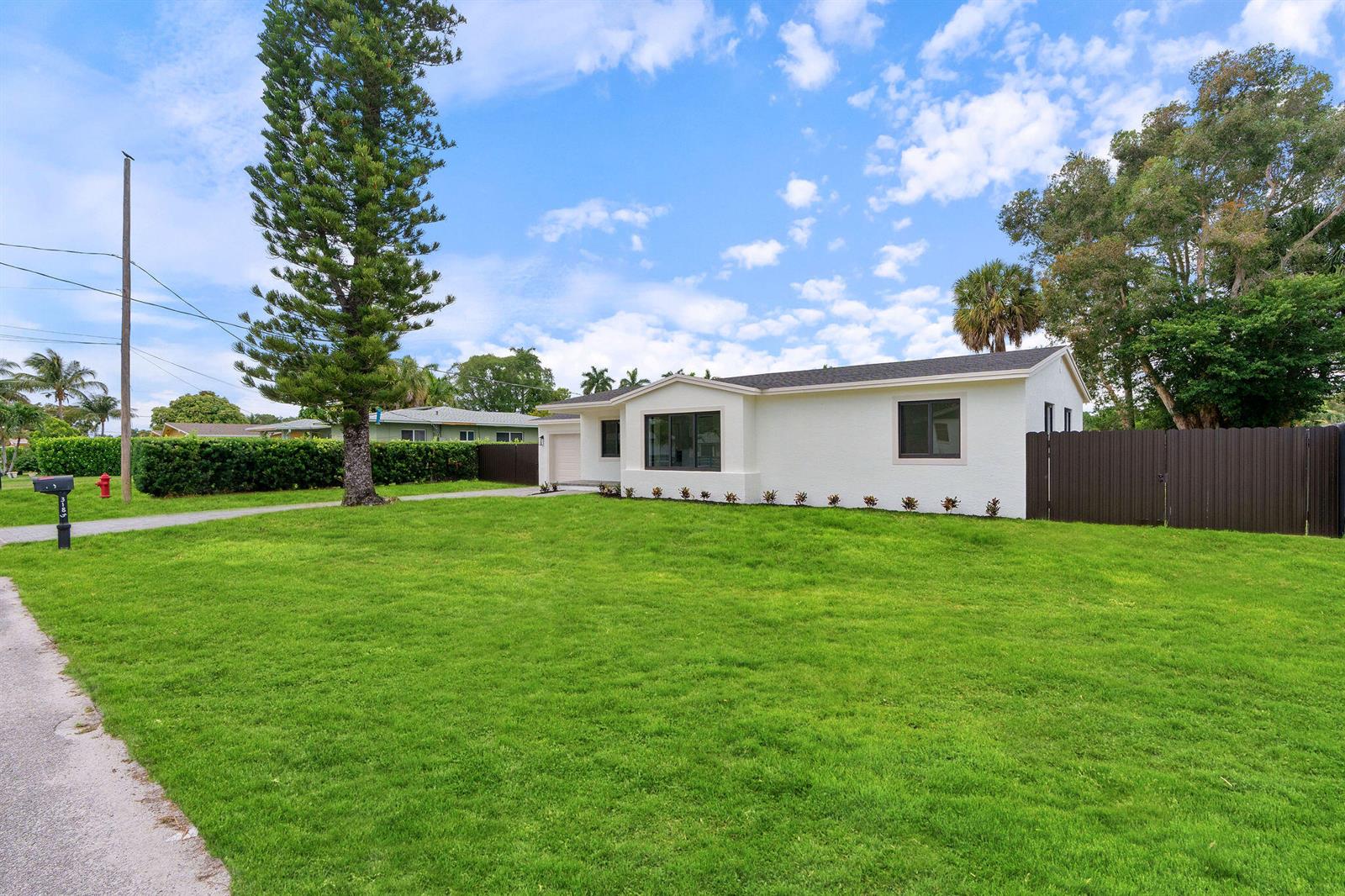 A white single-story house with a large green lawn and a dark brown privacy fence — 3185 Riddle Road, West Palm Beach FL 33406, WEST PALM BEACH, FL