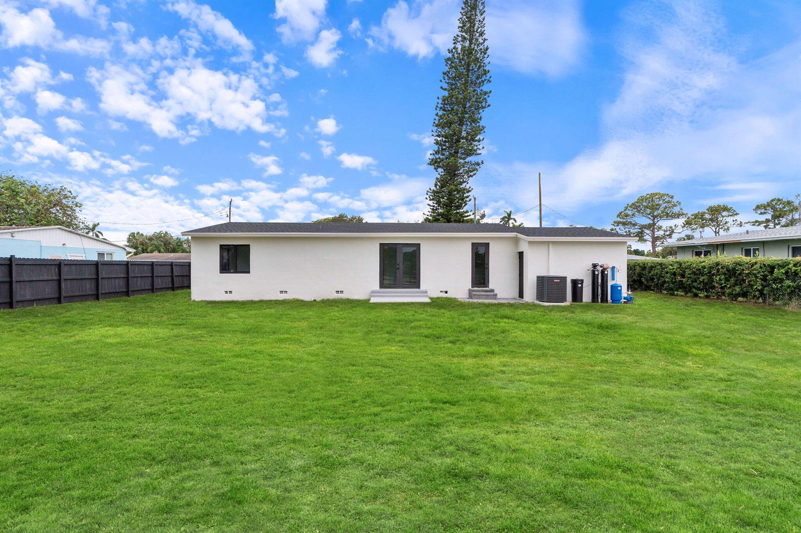 The exterior of a white, single-story house features a large backyard and a tall pine tree — 3185 Riddle Road, West Palm Beach FL 33406, WEST PALM BEACH, FL