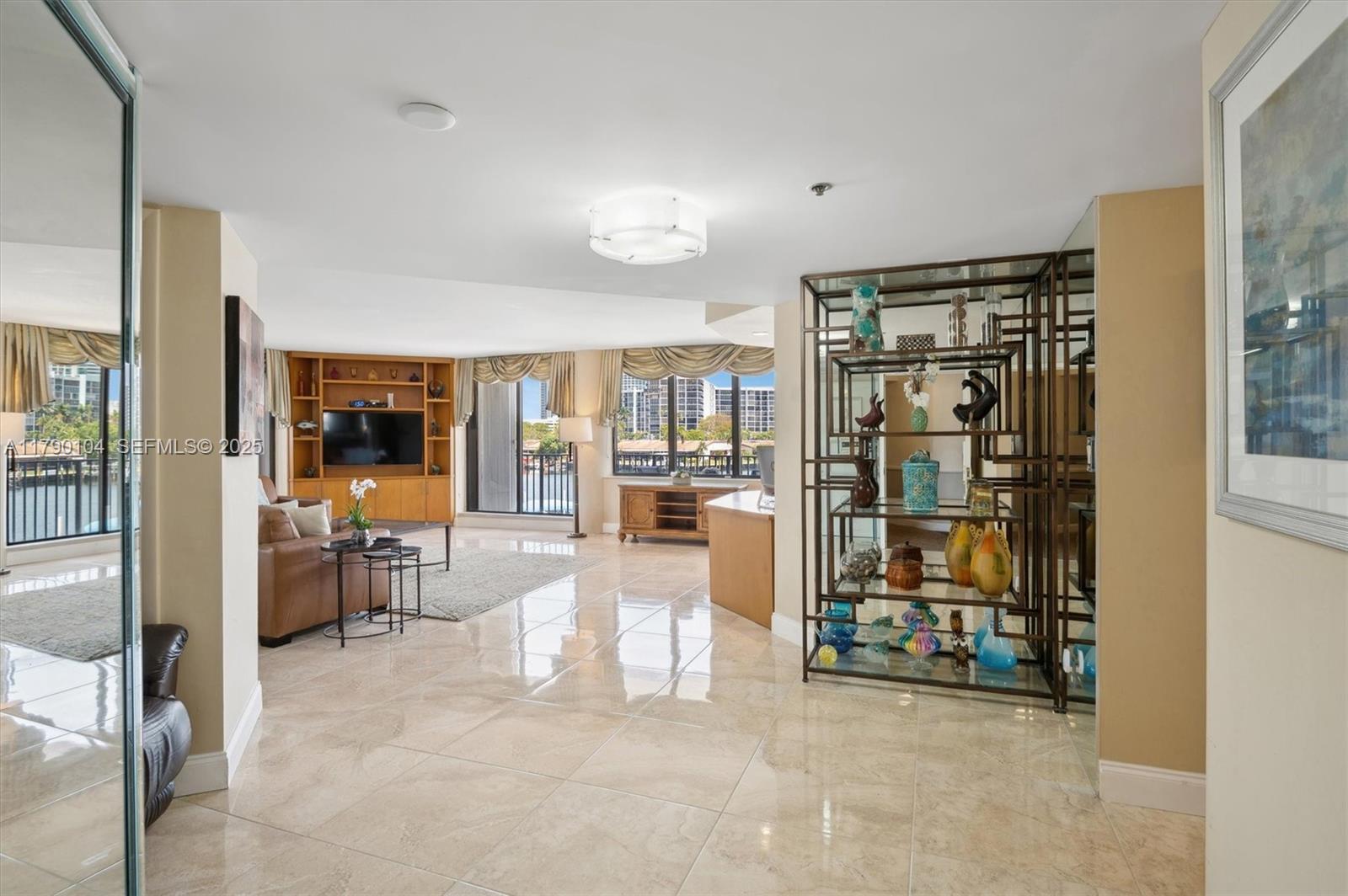 A spacious living room features tile floors, a large display shelf, and floor-to-ceiling windows — 300 Three Islands Blvd # 601, Hallandale Beach FL 33009, HALLANDALE BEACH, FL