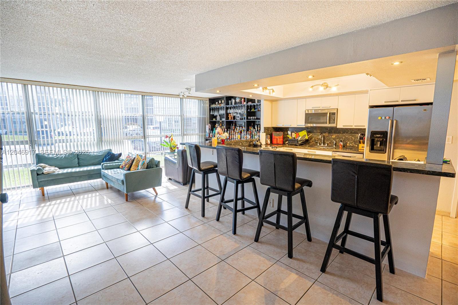 An open-concept kitchen with a breakfast bar and living area features tile flooring throughout — 601 Three Islands Blvd # 117, Hallandale Beach FL 33009, HALLANDALE BEACH, FL