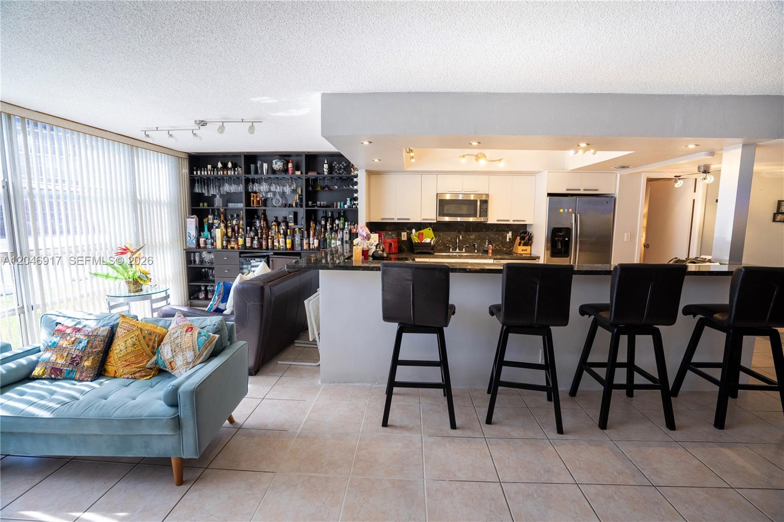 An open-concept kitchen features a breakfast bar with four stools, dark cabinetry, and tile flooring — 601 Three Islands Blvd # 117, Hallandale Beach FL 33009, HALLANDALE BEACH, FL