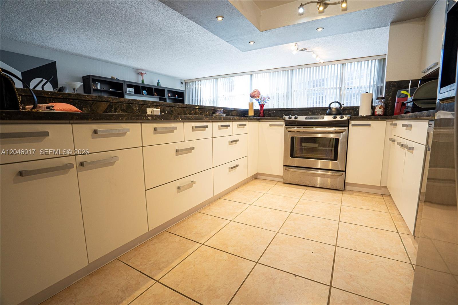 A kitchen features white cabinetry, dark countertops, stainless steel appliances, and beige tile flooring — 601 Three Islands Blvd # 117, Hallandale Beach FL 33009, HALLANDALE BEACH, FL