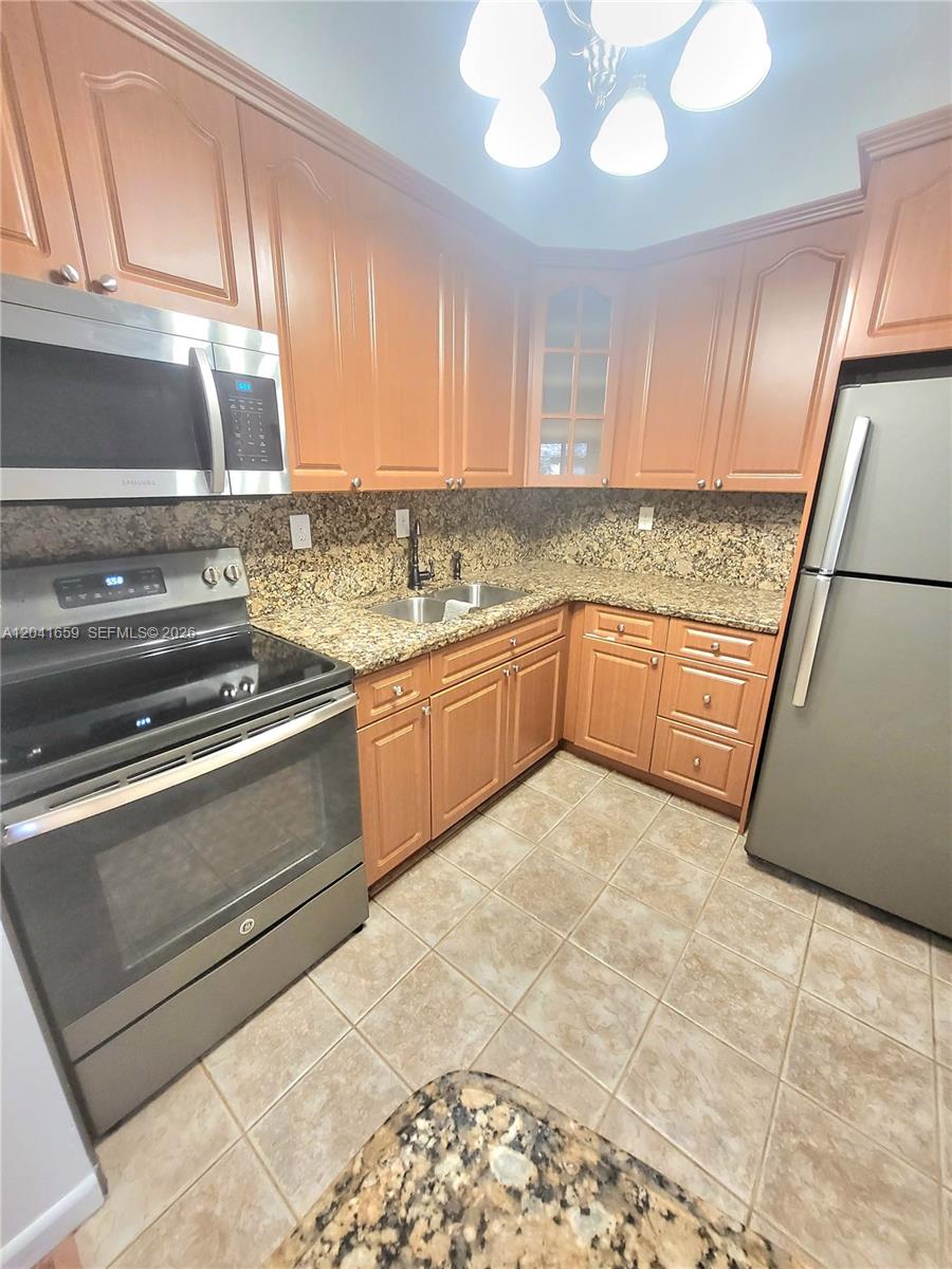 A kitchen features wood cabinets, granite countertops, stainless steel appliances, and light-colored tile flooring — 18845 NW 62nd Ave # 207, Hialeah FL 33015, HIALEAH, FL