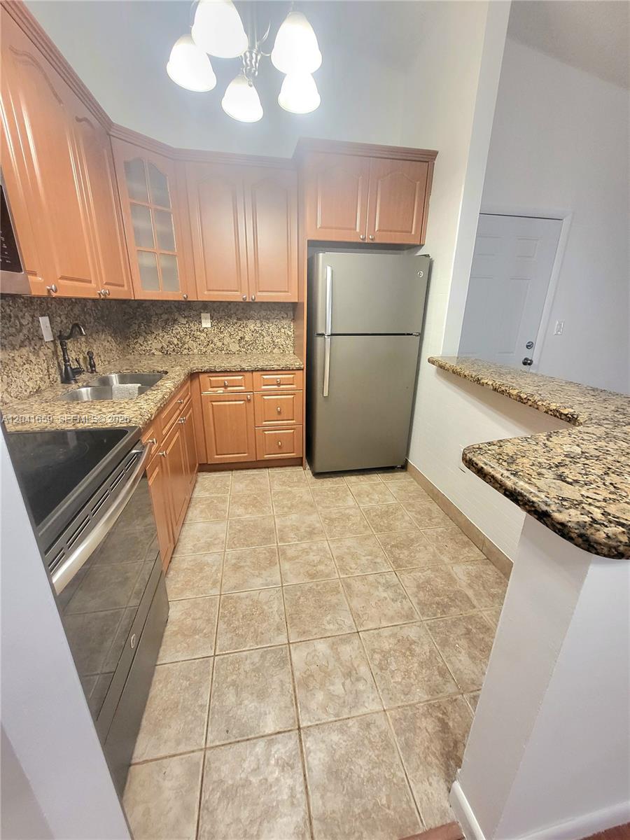 A kitchen features wood cabinets, granite countertops, stainless steel appliances, and tile flooring — 18845 NW 62nd Ave # 207, Hialeah FL 33015, HIALEAH, FL