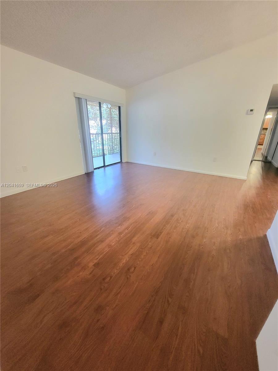 An empty room features wood-look flooring, white walls, and a sliding glass door to a balcony — 18845 NW 62nd Ave # 207, Hialeah FL 33015, HIALEAH, FL