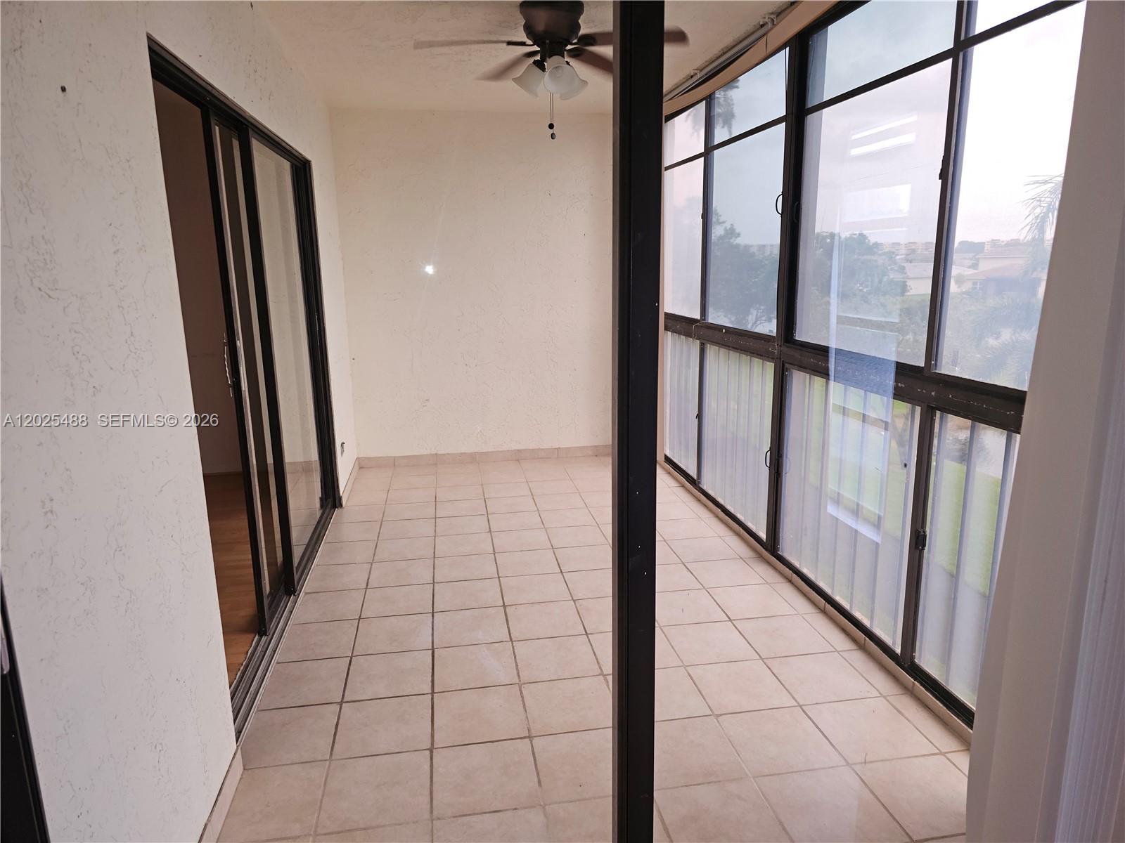 A tiled, enclosed balcony features a ceiling fan and large windows overlooking the outdoors — 7270 Ashford Pl # 308, Delray Beach FL 33446, DELRAY BEACH, FL