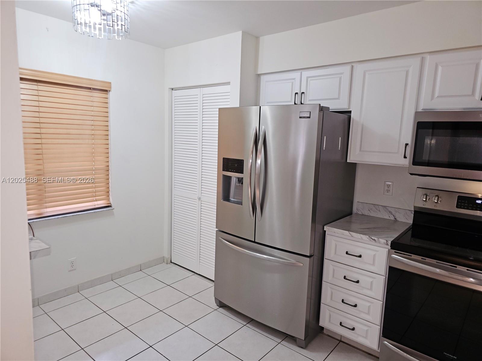 A kitchen features white cabinets, stainless steel appliances, a window with blinds, and tiled flooring — 7270 Ashford Pl # 308, Delray Beach FL 33446, DELRAY BEACH, FL