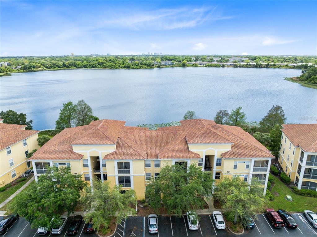 An aerial view shows a multi-story apartment building with a tile roof beside a lake — 1440 LAKE SHADOW CIRCLE UNIT 8305, MAITLAND, FL