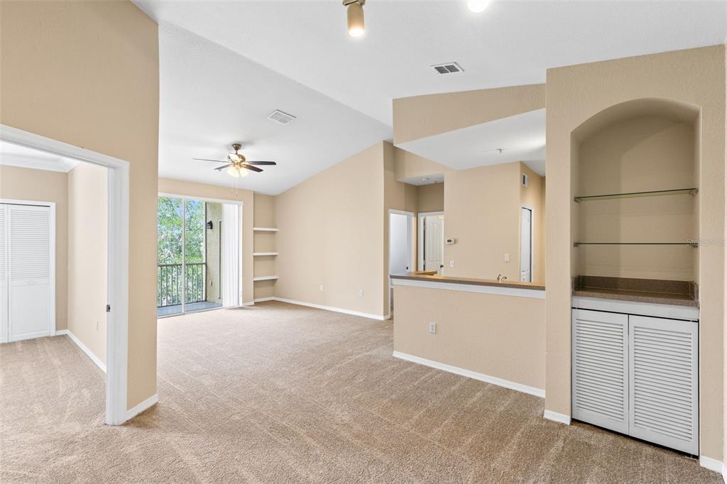An interior view of a living room with beige carpet, vaulted ceilings, and built-in shelving — 1440 LAKE SHADOW CIRCLE UNIT 8305, MAITLAND, FL