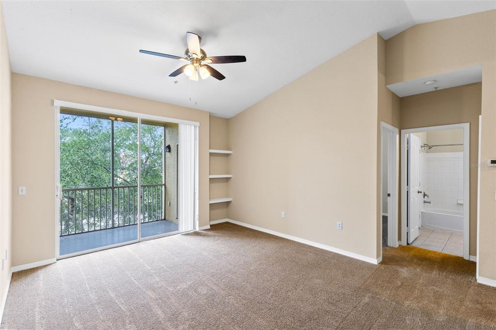 A bedroom with beige carpet, a ceiling fan, built-in shelves, and a sliding glass door — 1440 LAKE SHADOW CIRCLE UNIT 8305, MAITLAND, FL
